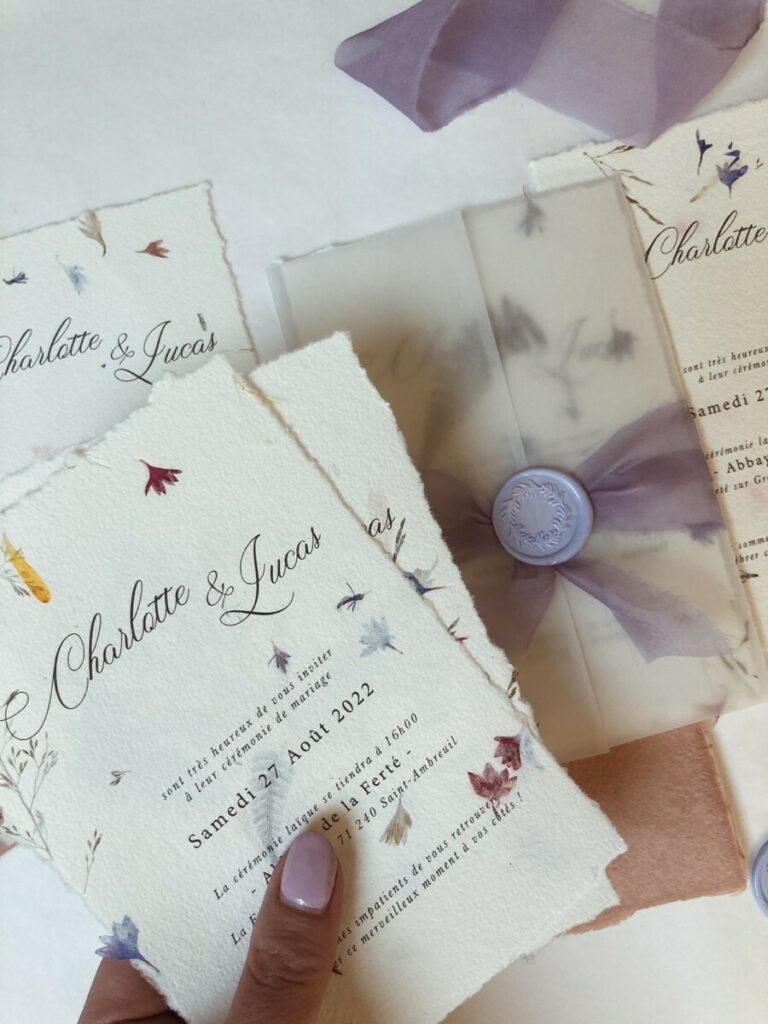 Faire-part de mariage avec papier fait main et inclusions de fleurs des champs – cachet de cire lavande – ruban mauve et pochette calque
