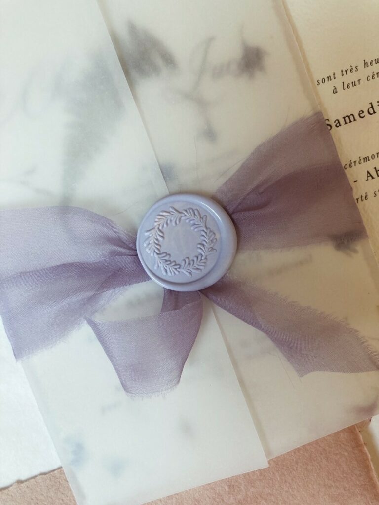 Faire-part de mariage avec papier fait main et inclusions de fleurs des champs – cachet de cire lavande – ruban mauve et pochette calque
