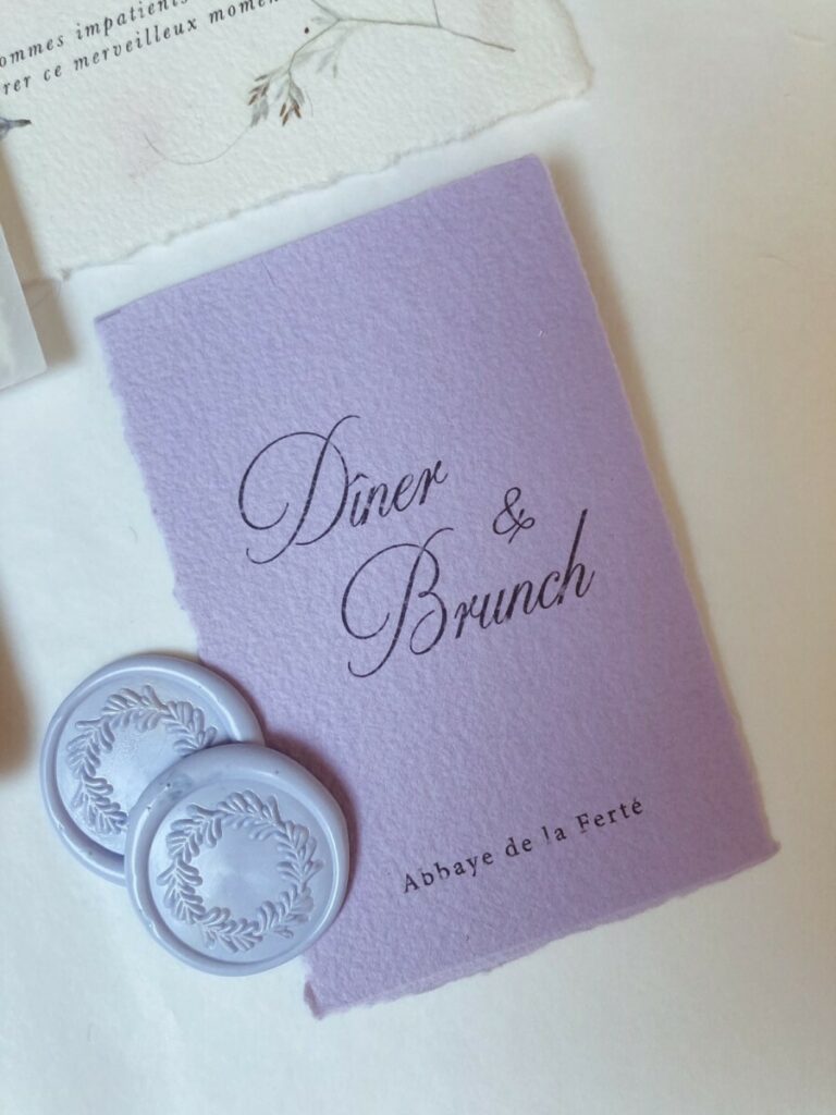 Faire-part de mariage avec papier fait main et inclusions de fleurs des champs – cachet de cire lavande – ruban mauve et pochette calque