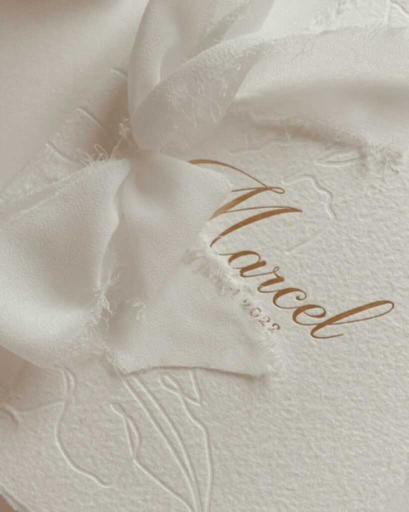 Faire-part de naissance bords frangés sur papier texturé Arches coton 400g – Marquage à chaud or mat et débossage pur – Ruban lin effiloché – cachet de cire blanc