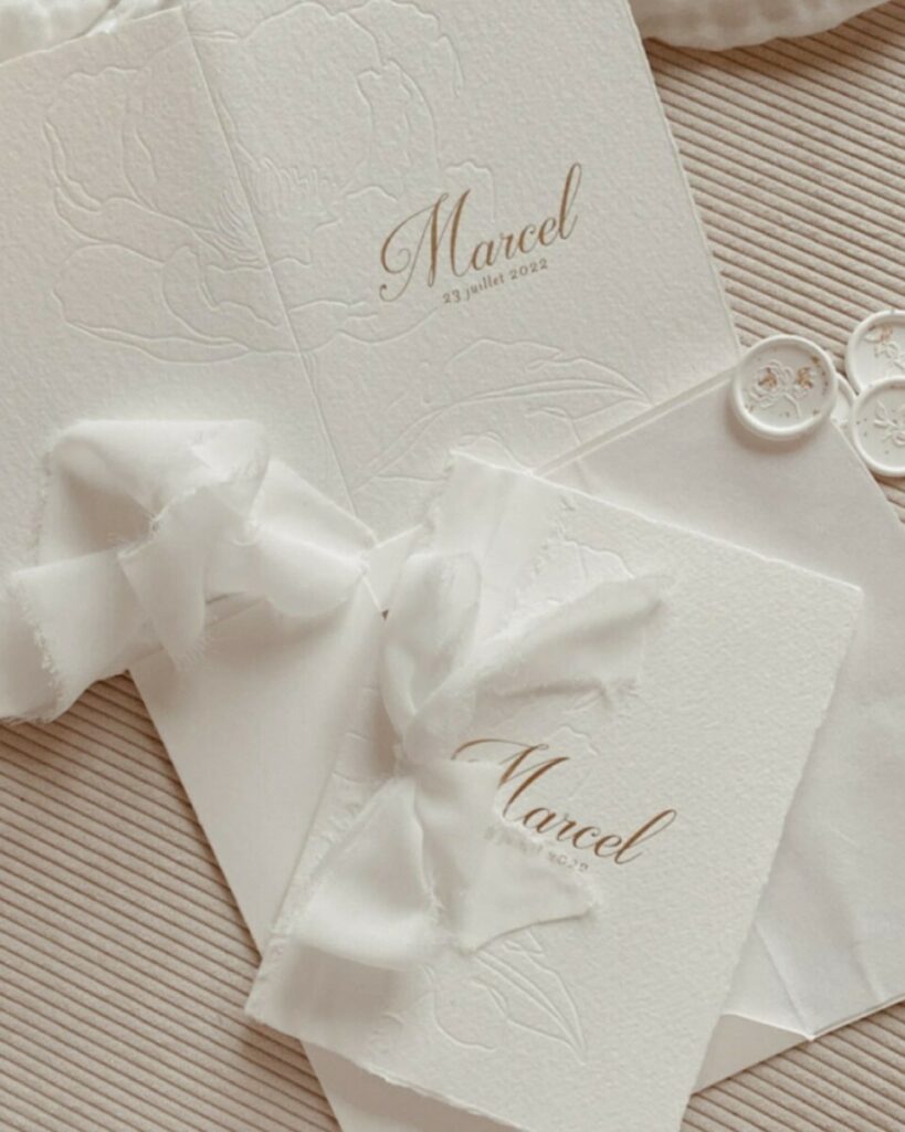 Faire-part de naissance bords frangés sur papier texturé Arches coton 400g – Marquage à chaud or mat et débossage pur – Ruban lin effiloché – cachet de cire blanc