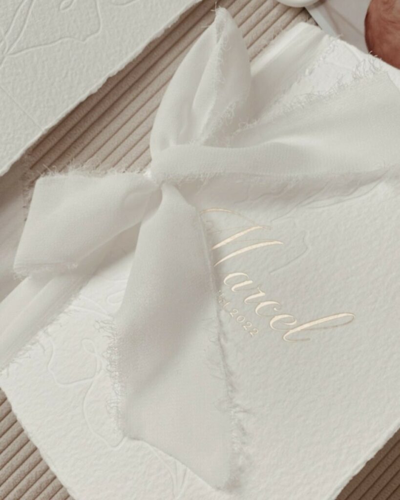 Faire-part de naissance bords frangés sur papier texturé Arches coton 400g – Marquage à chaud or mat et débossage pur – Ruban lin effiloché – cachet de cire blanc