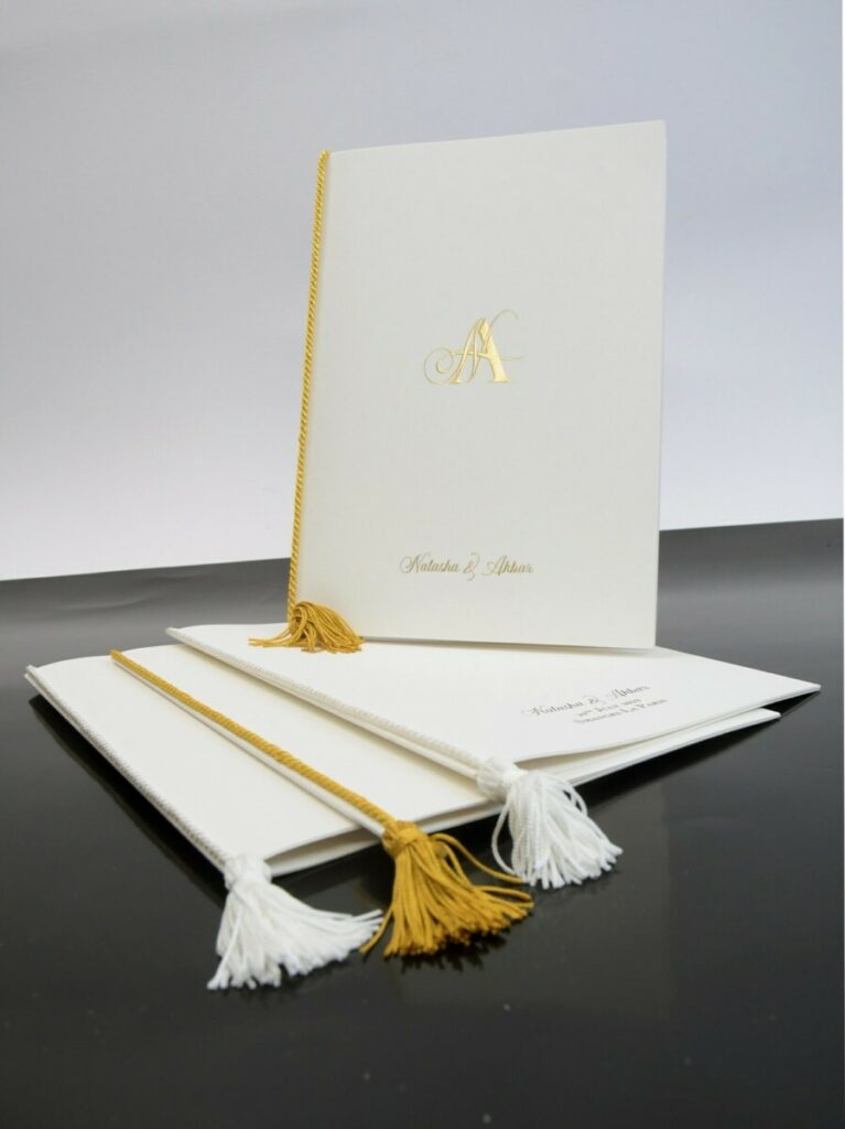 Menu livret pour cérémonie avec cordelière pompom assortie dorée – Old Mill Bianco 300gr/m2 – Monogramme en dorure galbée OR Mat