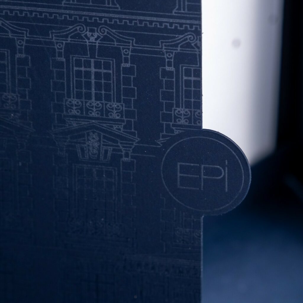 Carton d’invitation 50ans d’histoire avec une pochette a rabats et découpe sur mesure – Marquage à chaud transparent du château sur Sirio color dark blue – Invitation sur papier de création Vergé avec dorure à chaud or brilante