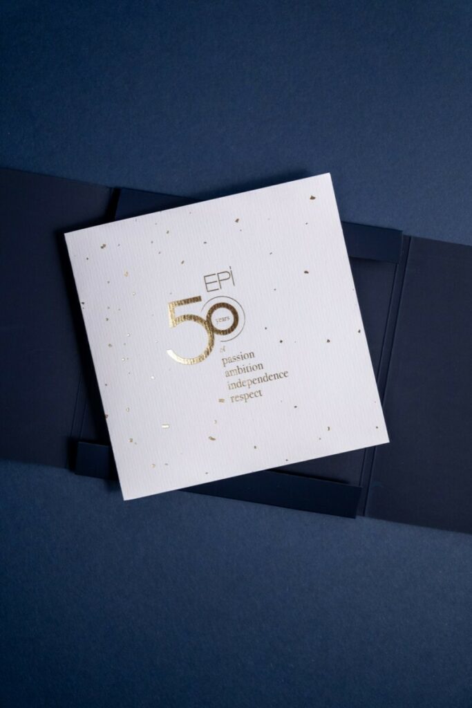 Carton d’invitation 50ans d’histoire avec une pochette a rabats et découpe sur mesure – Marquage à chaud transparent du château sur Sirio color dark blue – Invitation sur papier de création Vergé avec dorure à chaud or brilante