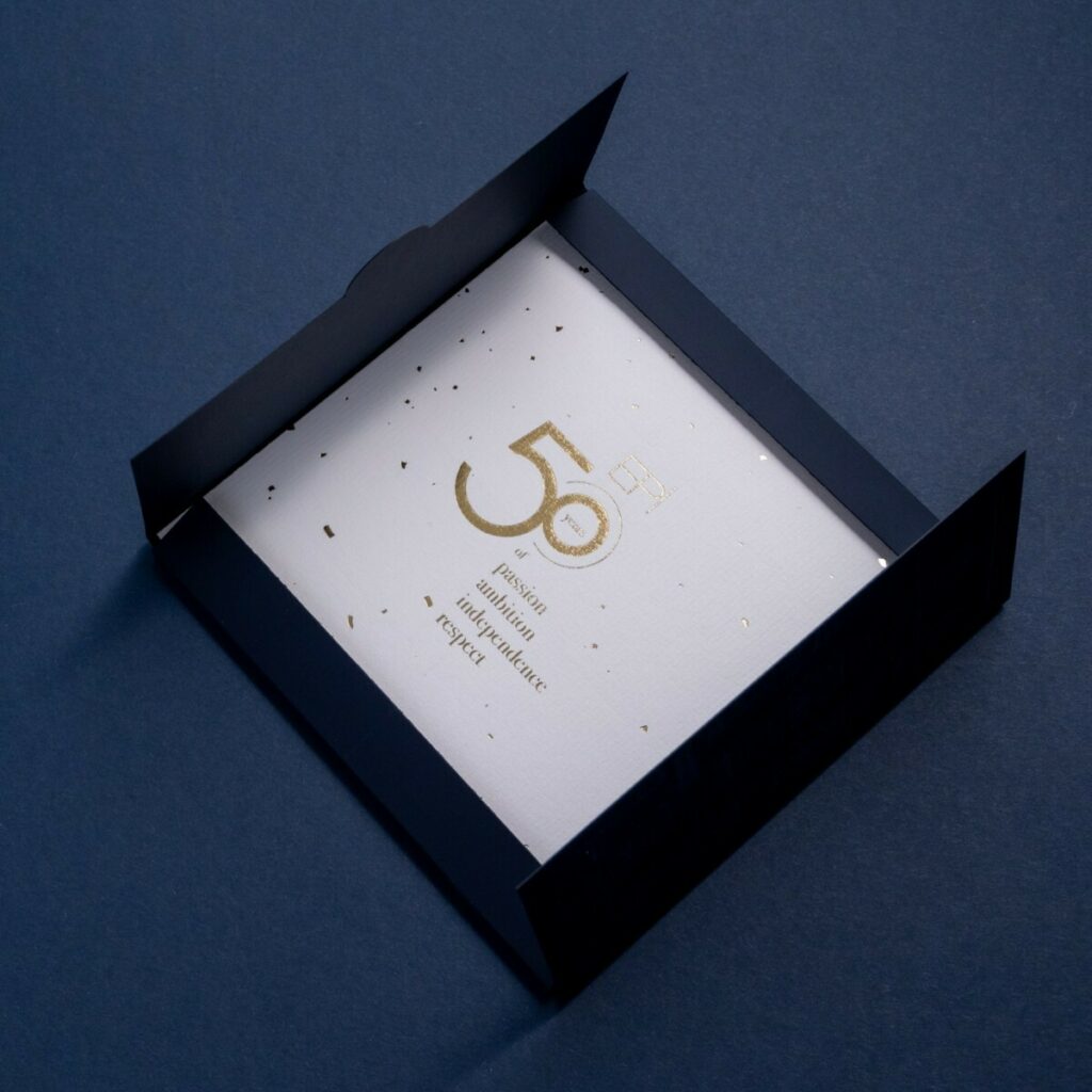 Carton d’invitation 50ans d’histoire avec une pochette a rabats et découpe sur mesure – Marquage à chaud transparent du château sur Sirio color dark blue – Invitation sur papier de création Vergé avec dorure à chaud or brilante